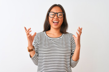Young chinese woman wearing striped t-shirt and glasses over isolated white background crazy and mad shouting and yelling with aggressive expression and arms raised. Frustration concept.