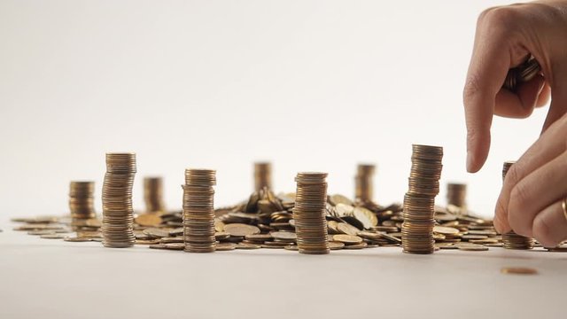 The concept of money. Columns of gold coins in the form of skyscrapers or Stonehenge. Close-up hands make up stacks of coins. Smoke. Garland.