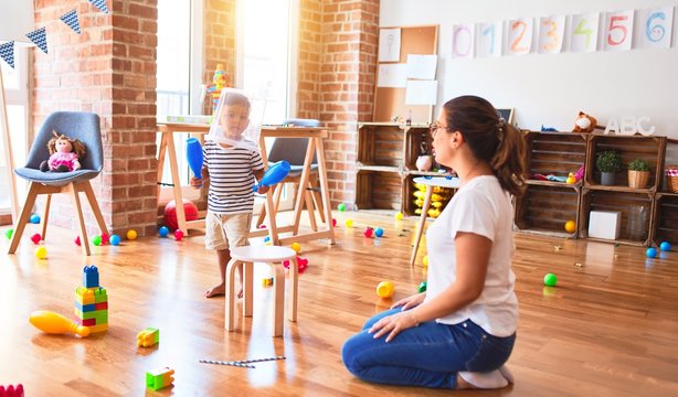 Beautiful teacher and toddler boy playing with plastic basket at kindergarten