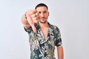 Young handsome man wearing Hawaiian summer shirt over isolated background looking unhappy and angry showing rejection and negative with thumbs down gesture. Bad expression.