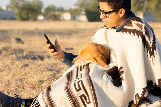 A man with his dog using his smartphone sitting in a grassy field
