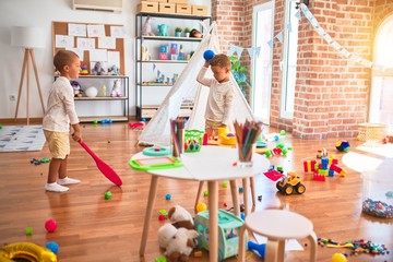 Adorable blonde twins playing around lots of toys at kindergarten