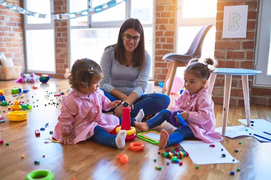 Young beautiful teacher and toddlers wearing uniform building pyramid using hoops at kindergarten