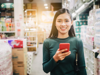 Young Asian holding mobile phone and look at camera, smile beautiful wearing green sweater at supermarket.