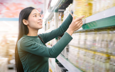 Young beautiful asian woman buying vegetable oil at grocery store, wearing green sweater.