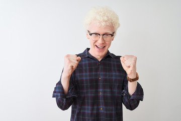Young albino blond man wearing casual shirt and glasses over isolated white background celebrating surprised and amazed for success with arms raised and open eyes. Winner concept.