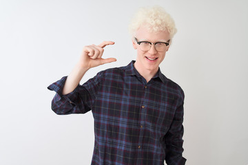 Young albino blond man wearing casual shirt and glasses over isolated white background smiling and confident gesturing with hand doing small size sign with fingers looking and the camera. Measure