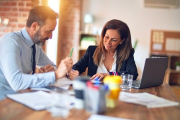 Two middle age business workers smiling happy and confident. Working together with smile on face using laptop at the office