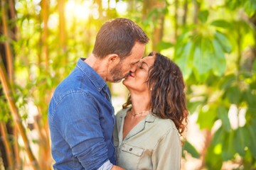 Middle age beautiful couple smiling happy and confident at town park. Standing with smile on face hugging and kissing