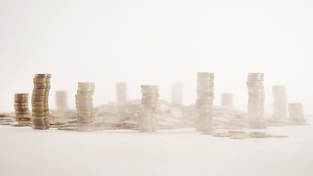 The concept of money. Columns of gold coins in the form of skyscrapers or Stonehenge. Close-up hands make up stacks of coins. Smoke. Garland.