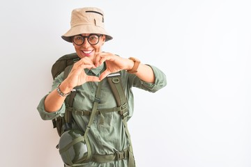 Middle age hiker woman wearing backpack canteen hat glasses over isolated white background smiling in love doing heart symbol shape with hands. Romantic concept.