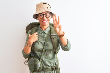 Middle age hiker woman wearing backpack canteen hat glasses over isolated white background showing and pointing up with fingers number three while smiling confident and happy.