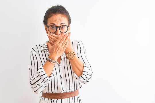 Middle age businesswoman wearing striped dress and glasses over isolated white background shocked covering mouth with hands for mistake. Secret concept.