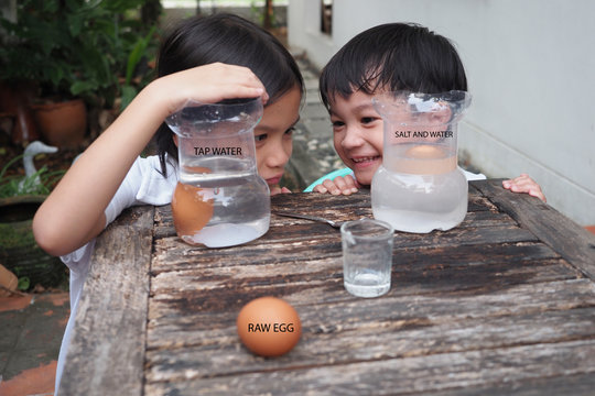 Kids Easy Experiment At Home.Asian Siblings Kid Making Salty Science With Floating Eggs In Water.Kid Put An Egg In Tap Water Versus Water That Added Enough Salt.Then They Observed For The Result,