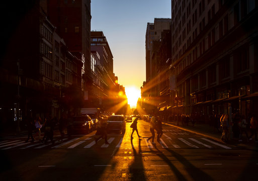 Crowds of people walk through the busy intersection at 23rd Street and Fifth Avenue in New York City with the bright light of sunset