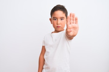 Beautiful kid boy wearing casual t-shirt standing over isolated white background doing stop sing with palm of the hand. Warning expression with negative and serious gesture on the face.