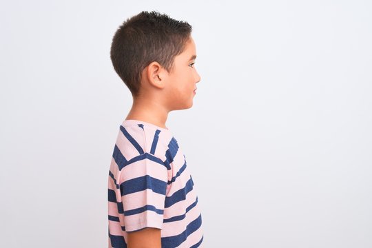 Beautiful kid boy wearing casual striped t-shirt standing over isolated white background looking to side, relax profile pose with natural face with confident smile.