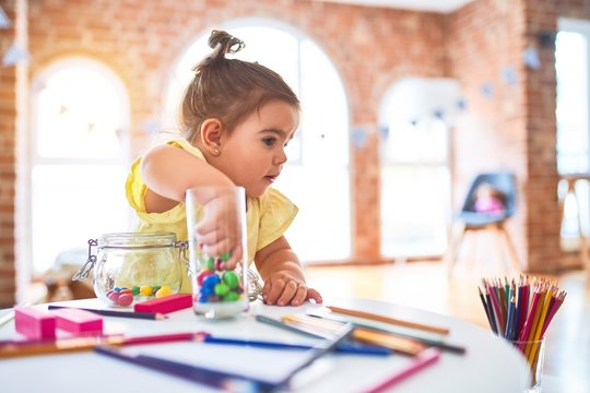 Beautiful toddler standing playing with chocolate colored balls on the table at kindergarten