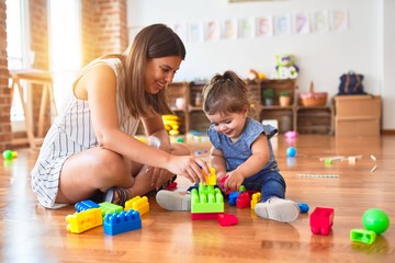 Young beautiful teacher and toddler playing with building blocks toy at kindergarten