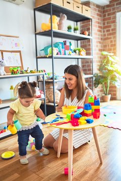 Young beautiful teacher and toddler playing with dishes, cutlery and cups toy on the table at kindergarten