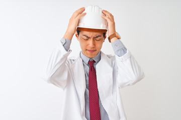 Chinese architect man wearing coat and helmet standing over isolated white background suffering from headache desperate and stressed because pain and migraine. Hands on head.