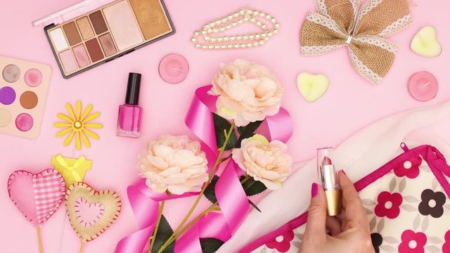 Women's cosmetics bag, cosmetics products and accessories appear on pink background and woman's hand put lipstick - Stop motion 
