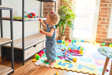 Beautiful caucasian infant playing with toys at colorful playroom. Happy and playful at kindergarten.