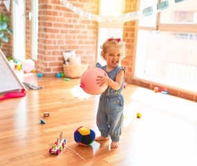 Beautiful caucasian infant playing with toys at colorful playroom. Happy and playful with pink baloon at kindergarten.