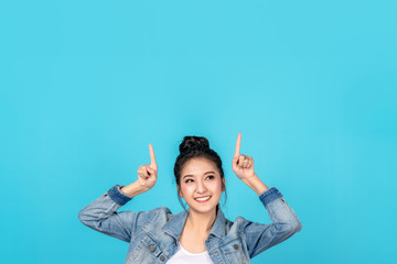 Happy asian woman feeling happiness and standing pointing hands up to copyspace on blue background.Cute asia girl smiling wearing casual jeans shirt and finger pointing to above for present promotions