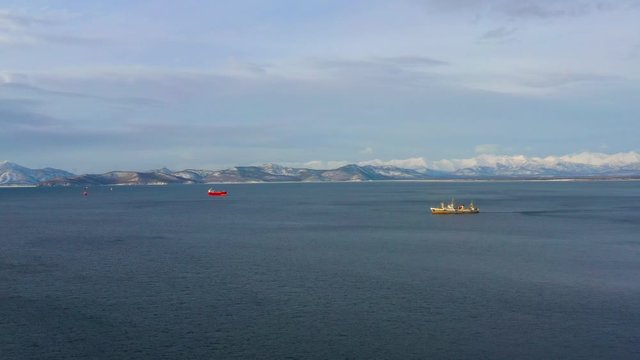 Fishing ship in the daytime sails on the Pacific ocean against the background of snow-capped mountains in Kamchatka, video from a quadrocopter