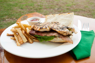 Sandwich prepared with grilled chicken with roast beef, french fries and tomato sauce, served outdoors on wooden table in Guatemala.