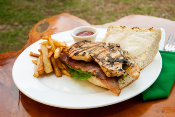  Sandwich prepared with grilled chicken with roast beef, french fries and tomato sauce, served outdoors on wooden table in Guatemala.