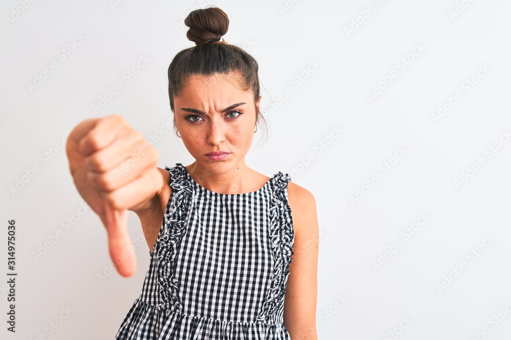 Poster Beautiful woman with bun wearing casual dresss standing over isolated white background looking unhappy and angry showing rejection and negative with thumbs down gesture. Bad expression.