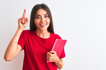 Young beautiful student woman holding red book standing over isolated white background surprised with an idea or question pointing finger with happy face, number one