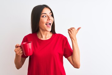 Young beautiful woman drinking red cup of coffee standing over isolated white background pointing and showing with thumb up to the side with happy face smiling