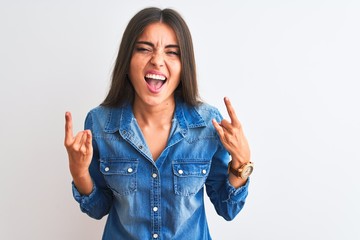 Young beautiful woman wearing casual denim shirt standing over isolated white background shouting with crazy expression doing rock symbol with hands up. Music star. Heavy concept.