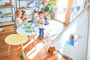 Beautiful teacher and group of toddlers playing around lots of toys at kindergarten