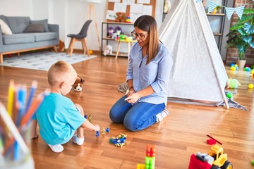 Young caucasian child playing at playschool with teacher. Playing with toy soldiers at playroom around toys.