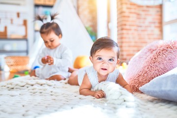 Beautiful infant happy girls playing together at home kindergarten lying on blanket