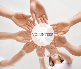 Team of young volunteers holding hands together on light background, bottom view