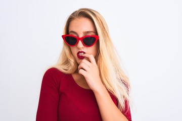 Young beautiful woman wearing red t-shirt and sunglasses over isolated white background looking stressed and nervous with hands on mouth biting nails. Anxiety problem.