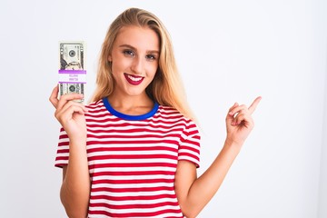 Obraz premium Beautiful woman wearing red striped t-shirt holding dollars over isolated white background very happy pointing with hand and finger to the side