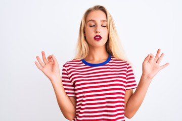 Young beautiful woman wearing red striped t-shirt standing over isolated white background relax and smiling with eyes closed doing meditation gesture with fingers. Yoga concept.
