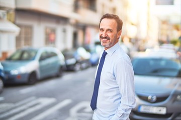 Middle age handsome businessman wearing shirt and tie standing on the street smiling