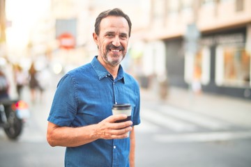 Middle age handsome man standing on the street drinking take away coffee smiling