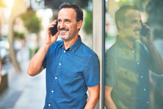 Middle age handsome businessman standing on the street talking on the smartphone smiling
