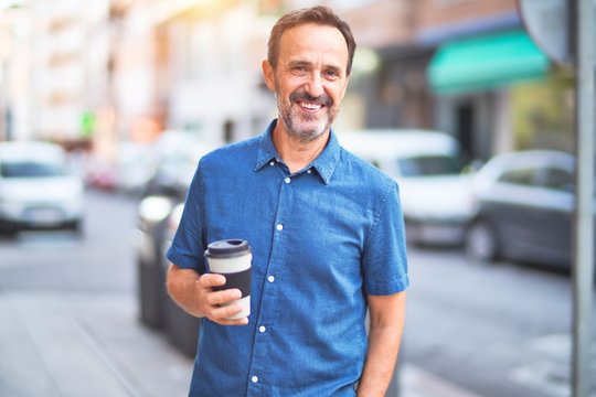 Middle age handsome man standing on the street drinking take away coffee smiling