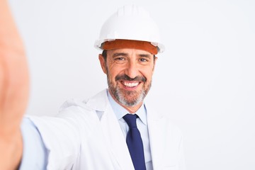 Middle age engineer man wearing helmet make selfie over isolated white background with a happy face standing and smiling with a confident smile showing teeth