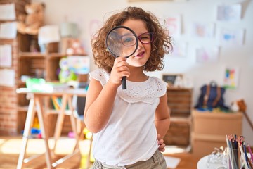 Beautiful toddler standing  wearing glasses using loupe at kindergarten