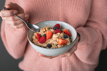 Woman in cozy pink sweater eating oatmeal porridge with berries. Concept of healthy eating, healthy...